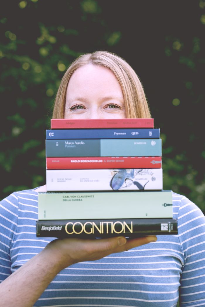 Una donna, Linda di Victu, seminascosta da una pila di libri tenuti in mano da un uomo